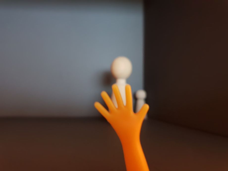 Orangefarbene Hand neben Holzfiguren – Symbol für Deeskalation und Schutz